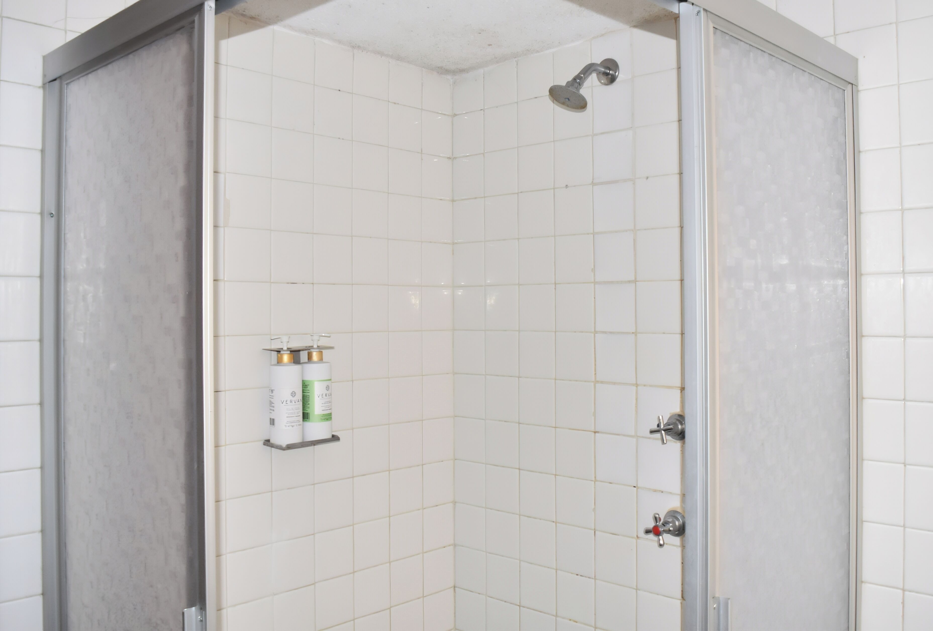 A shower with a handheld showerhead, a soap dispenser, and a water temperature control.
