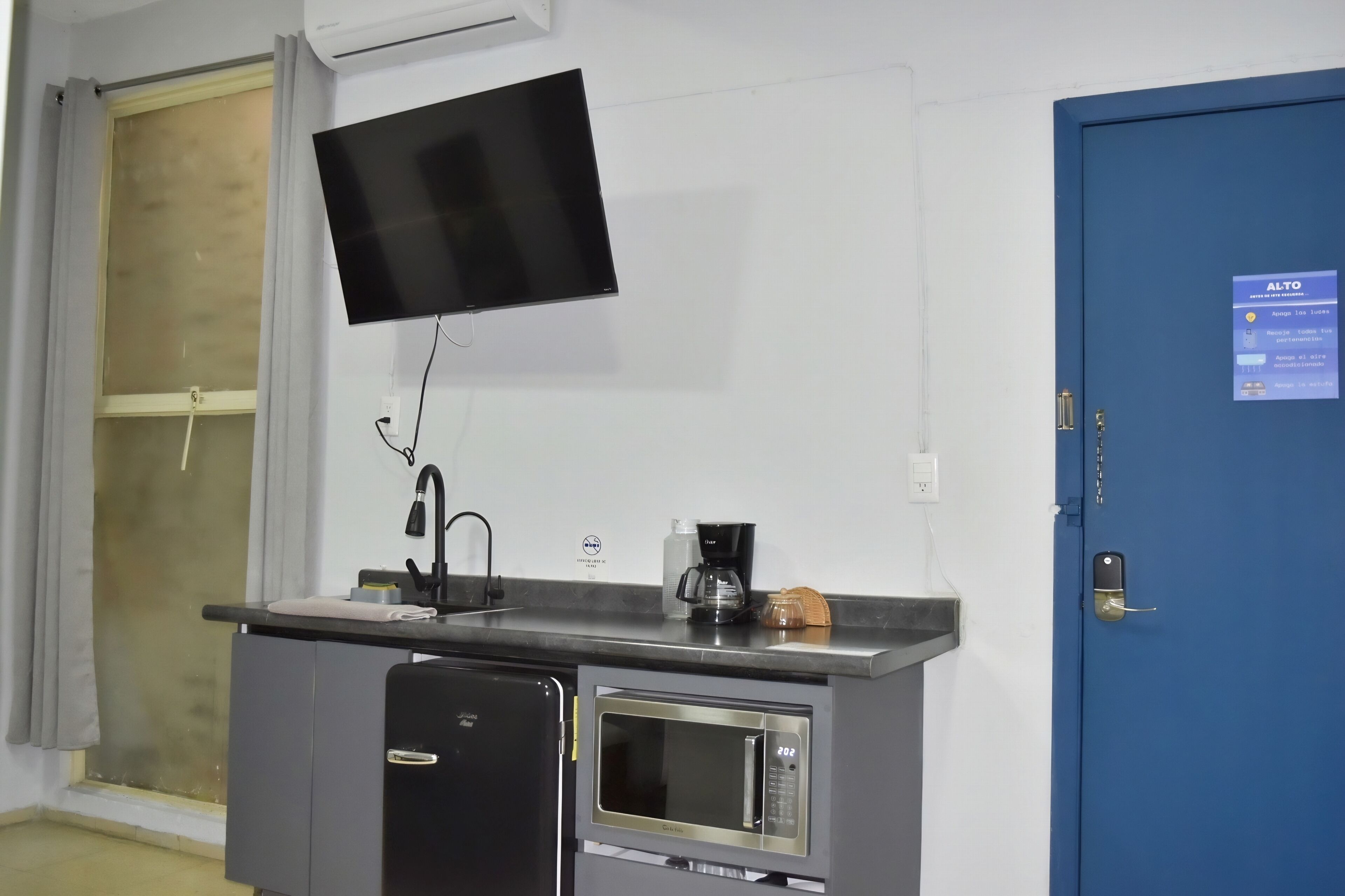 Une petite cuisine équipée d’un four à micro-ondes, d’une machine à café et d’un téléviseur à écran plat fixé au mur.