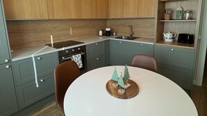 A modern kitchen with wooden cabinets, a white dining table, and pendant lights. - Magical and Cosy apartment with tree views from every window! (Rovaniemi)