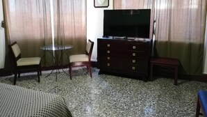 Habitación de hotel con televisión, una mesita redonda, dos sillas, un banco de madera y una cama.
