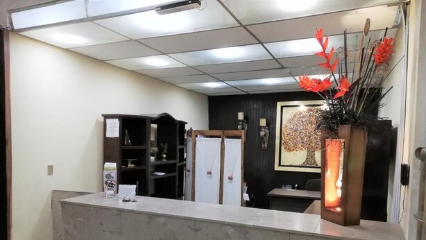 Zona de recepción con mostrador de mármol, un tablón de anuncios, perchero y un jarrón decorativo con flores rojas.