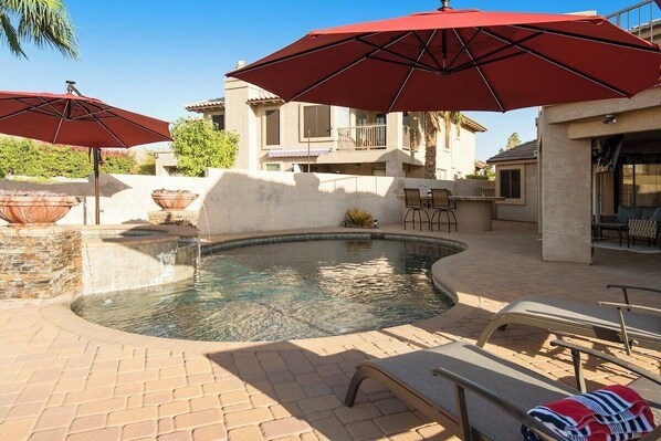 A swimming pool with two red umbrellas, lounge chairs, and a stone wall. - Spectacular Lake House Retreat (Glendale)