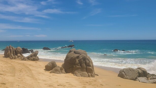 A sandy beach with large rock formations and the ocean.