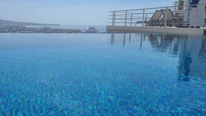 A clear infinity pool with a cityscape view, including a mountain and buildings.