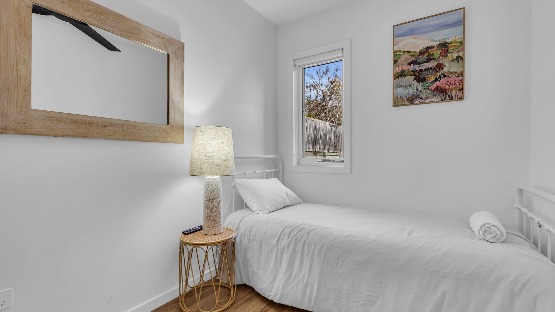 A bedroom with a bed, a bedside lamp, a window, and a painting on the wall.
