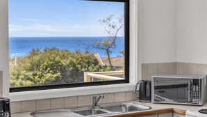 A kitchen with a view of the ocean, a sink, a kettle, and a microwave. - Sapphire Tides - Stunning Views (Tura Beach)