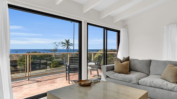 A balcony with a view of the ocean, a grey sofa, and a wooden bowl on a table. - Sapphire Tides - Stunning Views (Tura Beach)