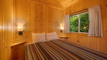 A wooden-paneled room with a bed, two bedside lamps, and a window with curtains.