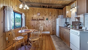 A wooden interior with a dining table, chairs, a stove, and a refrigerator. - 2BR Beach Cabin on prime west-facing beach! (Eastsound)
