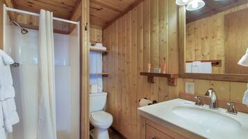 Bagno con rivestimento in legno, doccia, WC e lavandino.