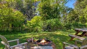 A backyard with a fire pit, two Adirondack chairs, and a picnic table.