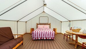 A tented room with a bed, a sofa, and a table with chairs.