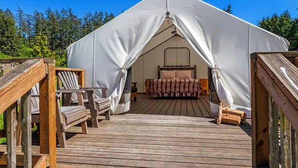 A tent with a bed inside, surrounded by a wooden deck and chairs.