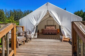 A tent with a bed inside, surrounded by a wooden deck and chairs.