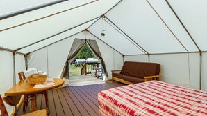 A tent with a bed, a table, and a chair. There is a view of the outside through a window.