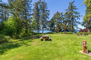 Zona de picnic con mesa y bancos de madera, rodeada de árboles altos y vista al agua.