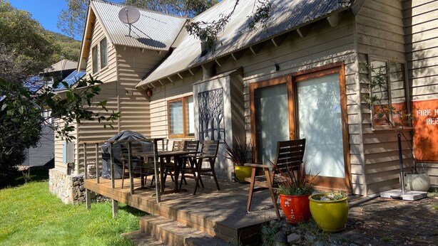 Uma casa de madeira com varanda coberta, móveis de exterior e plantas em vasos.
