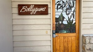 Uma porta de madeira com um painel de vidro com um desenho de folha, uma placa de madeira acima da porta com a inscrição "Bollygums" e o número "6" na parede.