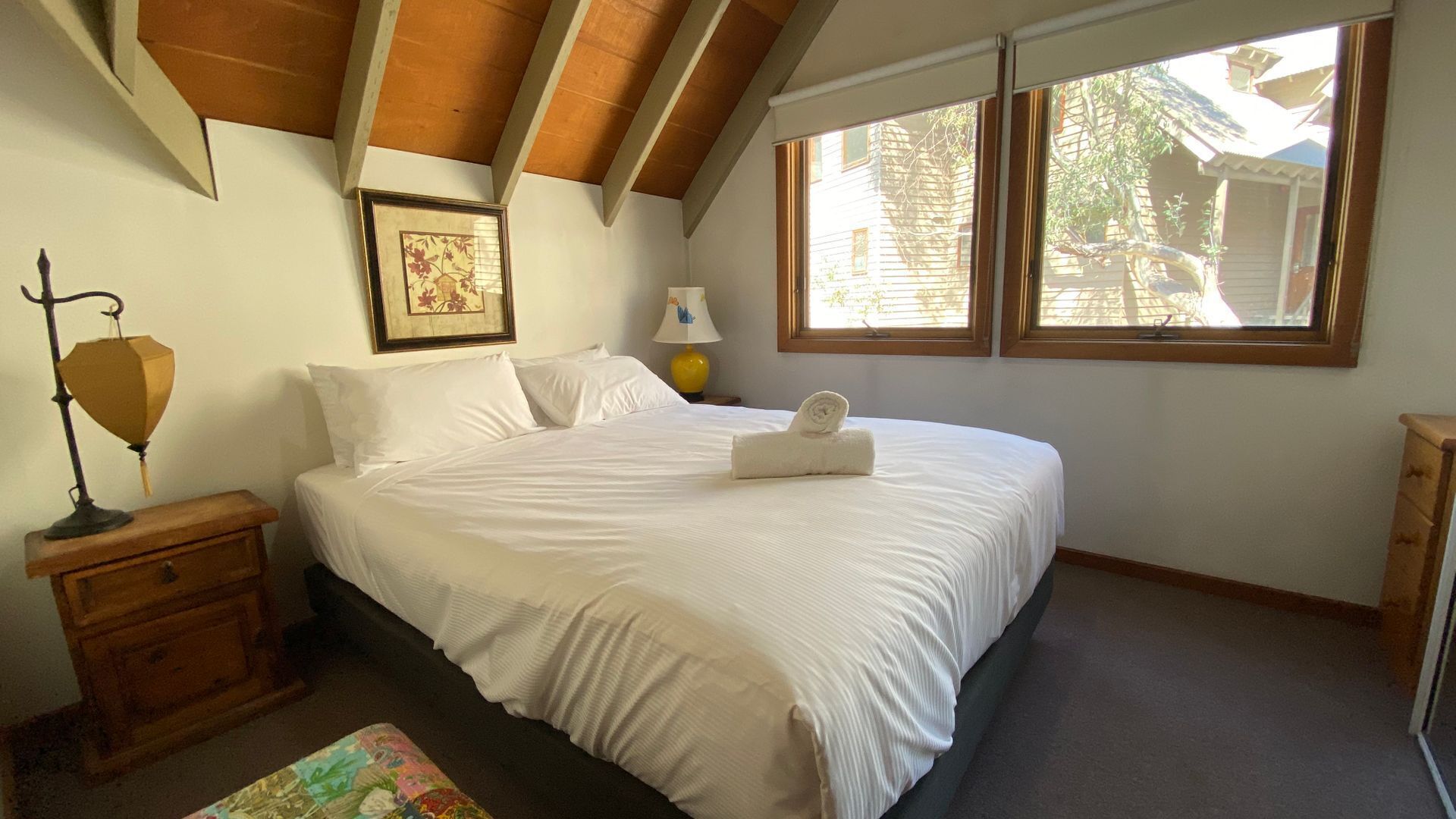 A bedroom with a bed, a nightstand, a lamp, a framed picture, and a window.