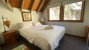 Um quarto com uma cama, mesa de cabeceira, abajur, quadro e janela.