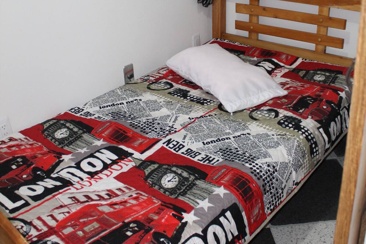 Ein Einzelbett mit einem gemusterten Bettbezug, einem weißen Kissen und einem hölzernen Kopfteil.