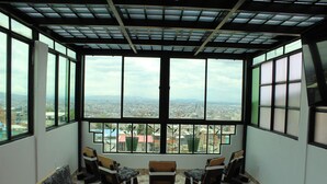 Ein Zimmer mit großen Fenstern und Blick auf die Stadt, ausgestattet mit einer Sitzecke mit Sesseln und einem Fliesenboden.