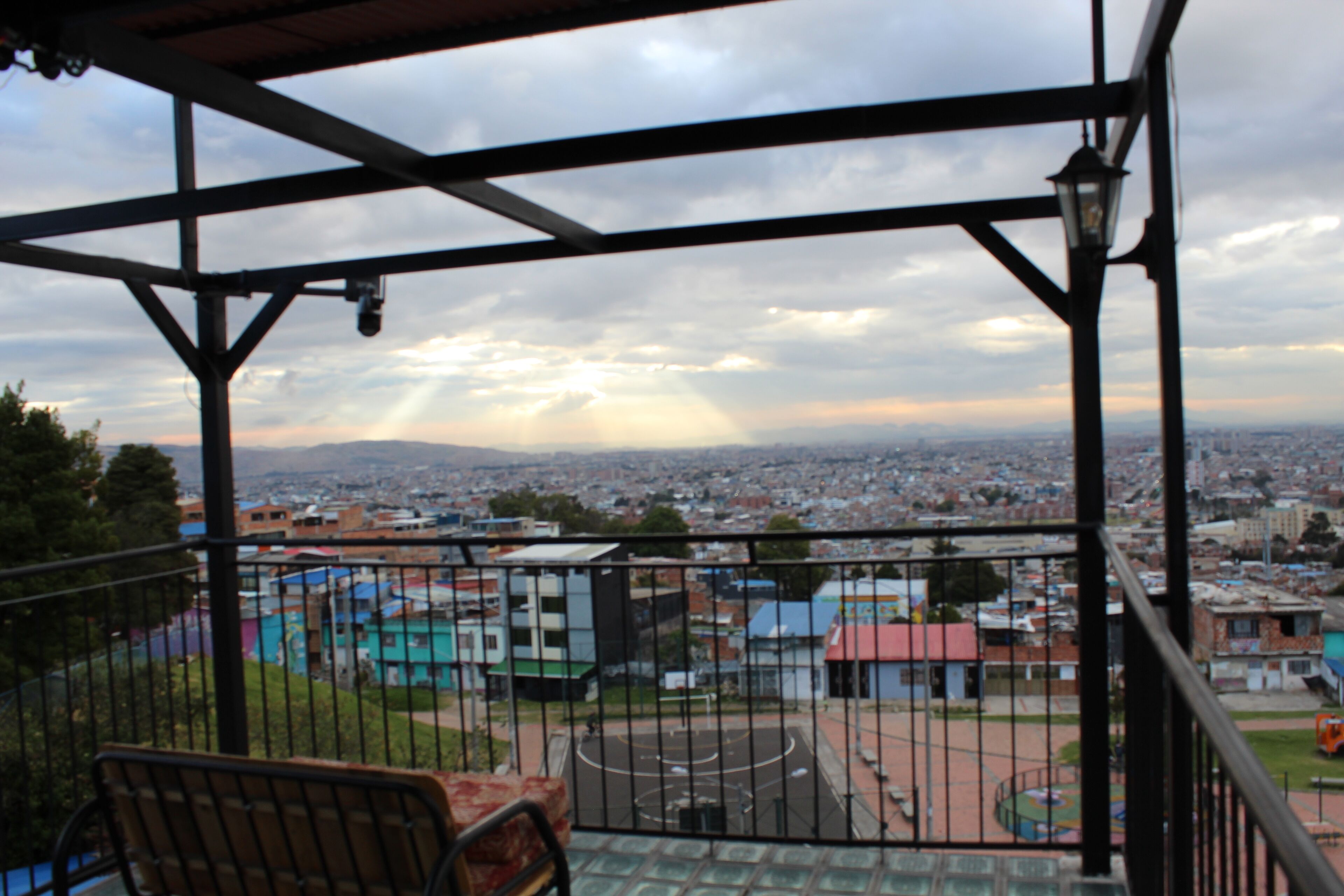 Varanda com guarda-corrimão de metal vista para a paisagem urbana com edifícios e um parquinho.
