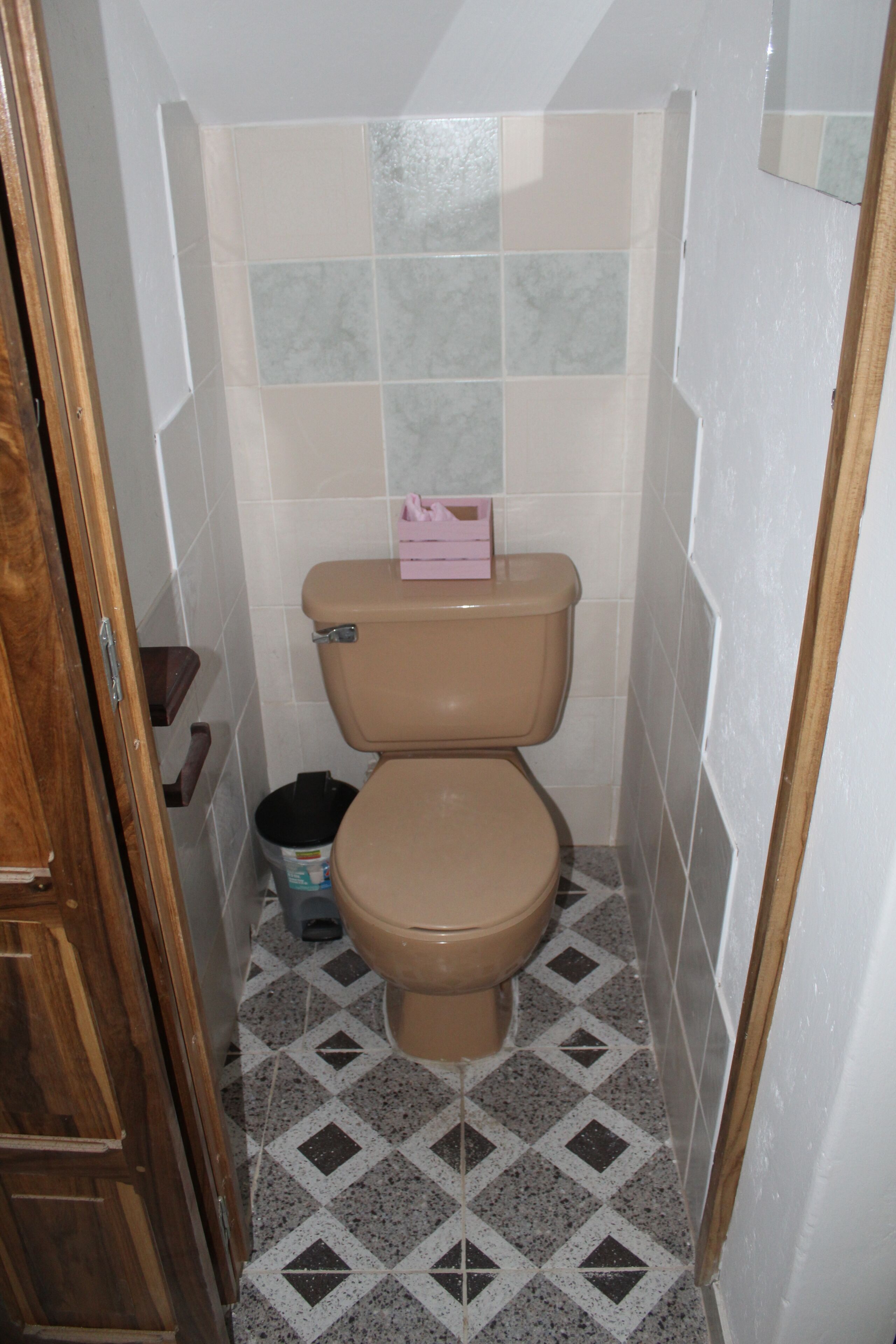 Une petite salle de bain avec des toilettes, une poubelle et une porte en bois.