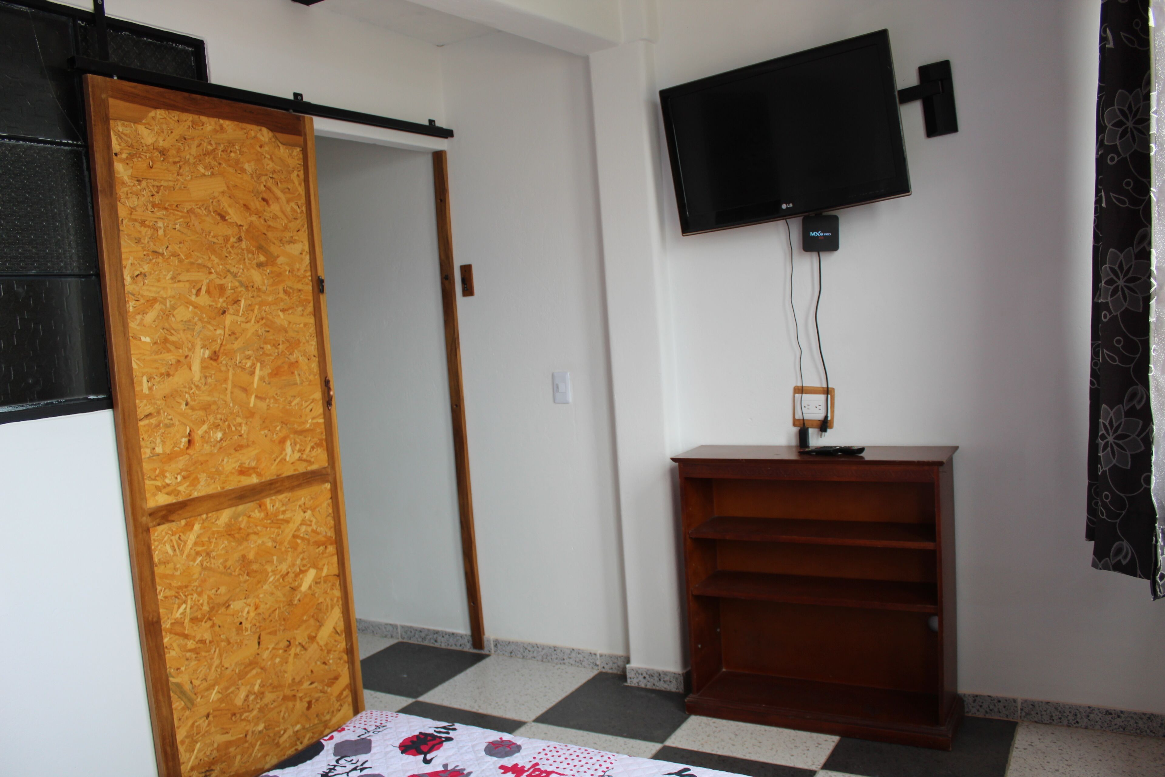 A room with a wooden door, a television mounted on the wall, and a wooden shelf.