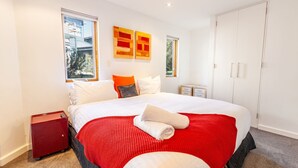 Ein modernes Schlafzimmer mit einem großen Bett, zwei Fenstern, einem Kleiderschrank und einem Nachttisch in Rot.