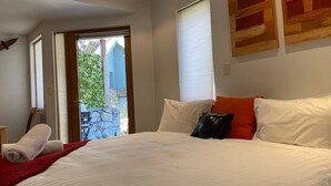 Quarto com uma cama grande, manta vermelha e vista para uma parede de pedra e vegetação lá fora.