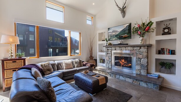 Ein modernes Wohnzimmer mit Kamin aus Stein, einem großen Ecksofa und einem an der Wand befestigten Fernseher.