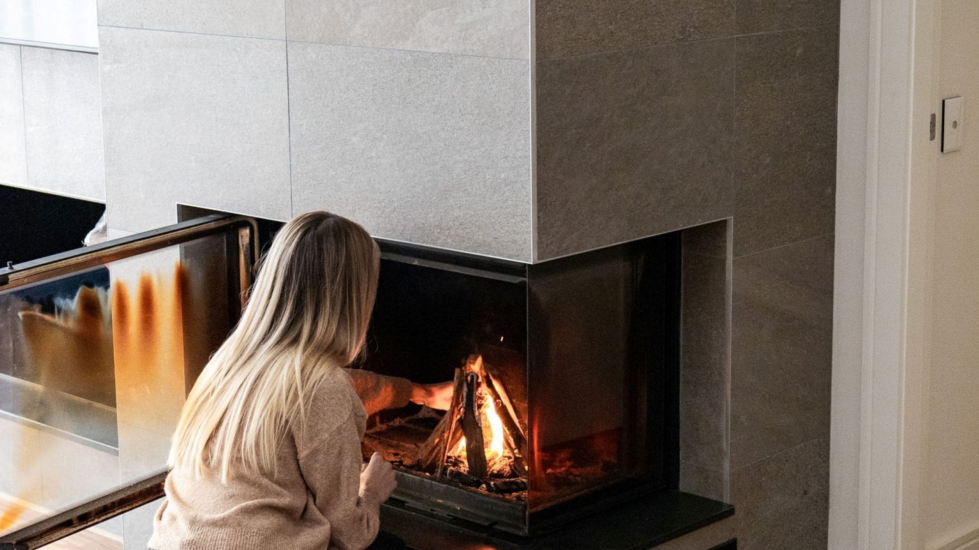 A person standing in front of a modern fireplace with a glass enclosure.