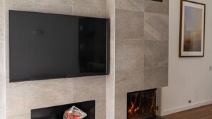 Un salon moderne avec un téléviseur à écran plat fixé sur un mur en pierre, une cheminée avec un feu visible et un tableau encadré accroché au mur.