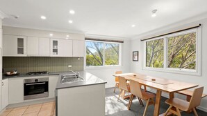 Una cocina moderna con comedor, ventanas amplias y vistas a árboles.