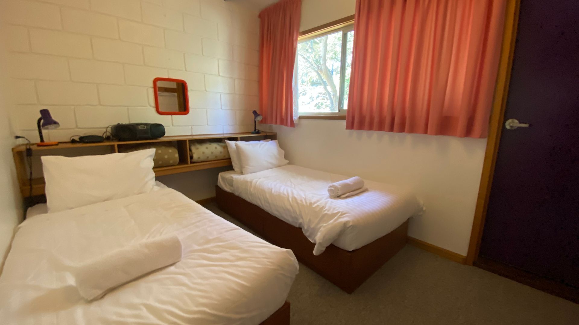 A room with two beds, a mirror, a window with curtains, and a door.