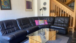 Ein schwarzes, ledernes Ecksofa mit einem Glastisch, einem Holznachttisch und einem farbenfrohen, abstrakten Gemälde an der Wand.