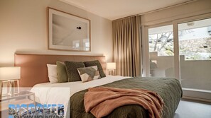 Relax in this serene hotel room featuring a large bed, framed artwork, and a window with a scenic view.