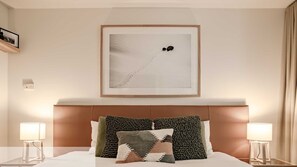 Ein Hotelzimmer mit einem Bett, zwei Nachttischlampen, einem gerahmten Bild an der Wand und einem Kopfteil mit dekorativen Kissen.