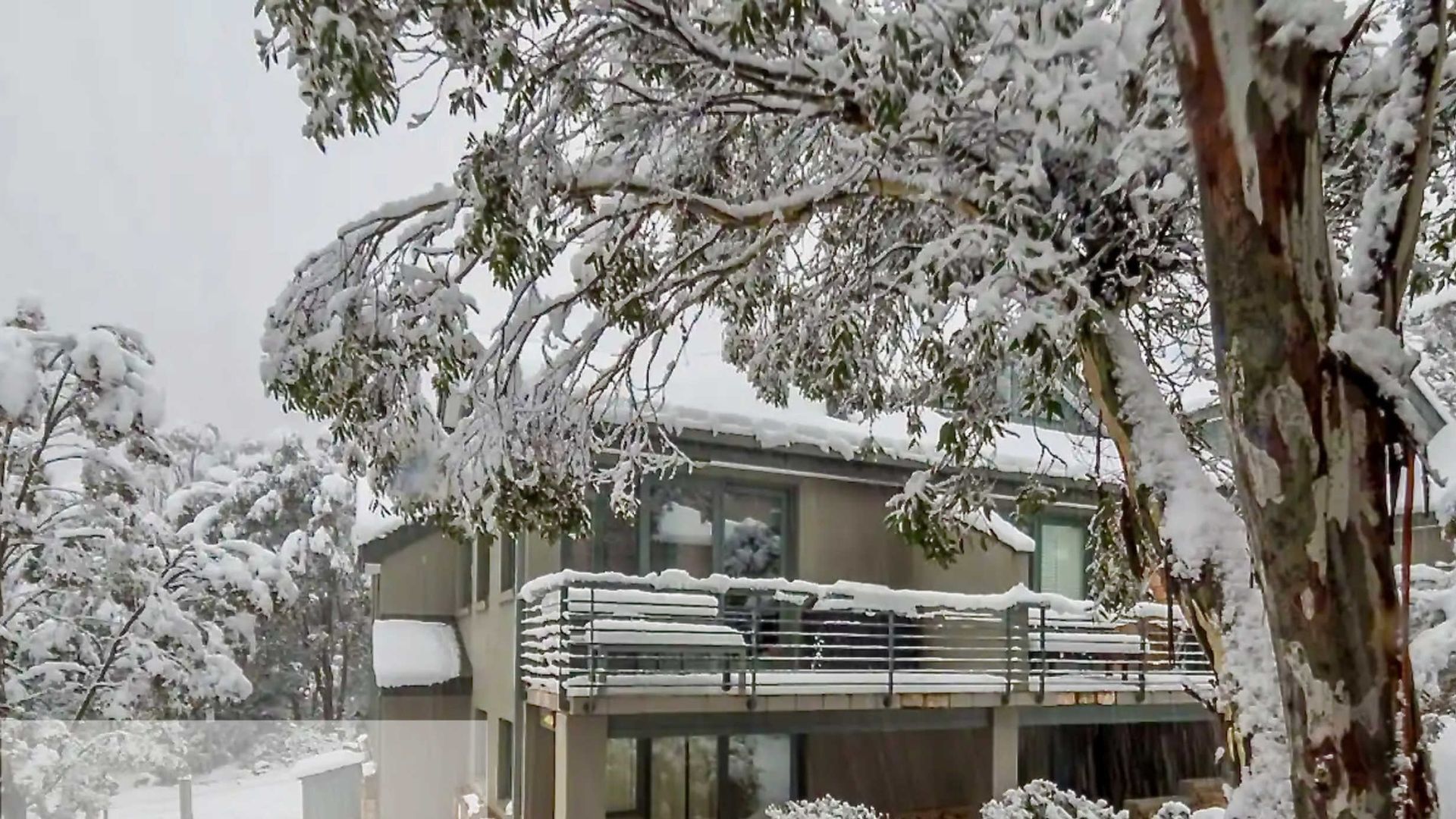 A residential building with a balcony covered in snow, surrounded by snow-covered trees.