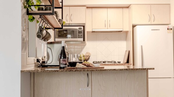 A kitchen with a built-in microwave, a gas stove, and a refrigerator. There is a wine bottle and glasses on the counter.