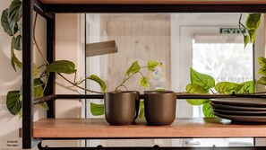 A shelf with two ceramic cups and a plate, a potted plant, and a wooden shelf.