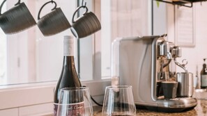A kitchen counter with a wine bottle and two glasses, a coffee machine, and hanging pots.