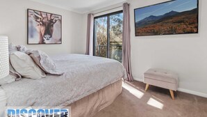 A bedroom with a large bed, a window with curtains, a small bench, and two framed pictures on the wall. - Snow Creek 4 - Thredbo (Thredbo)