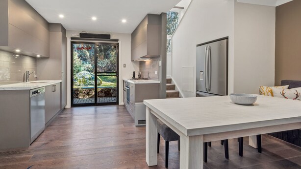 A modern kitchen with a large island, built-in appliances, and a view through a glass door to a garden. - Snow Creek 4 - Thredbo (Thredbo)