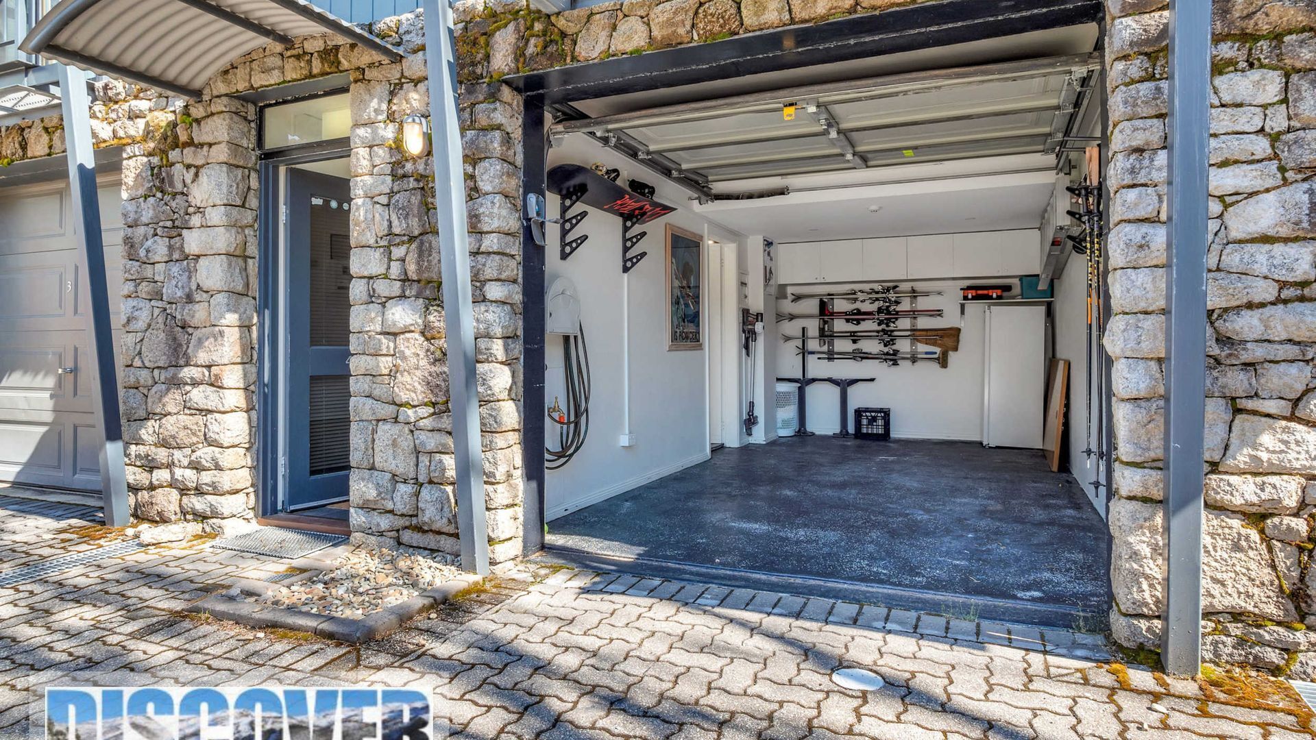 A stone building with a garage entrance, a ski rack, and a door with a number '3'.