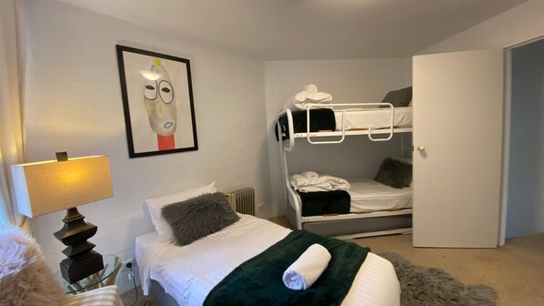 A room with a bunk bed, a single bed, a lamp, a radiator, and a framed picture on the wall. - Sitzmark 1 - Central Village location (Thredbo)