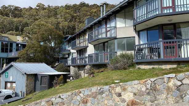 A multi-story building with balconies, stone walls, and a grassy slope. - Sitzmark 1 - Central Village location (Thredbo)