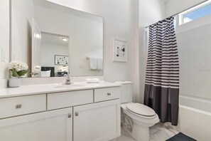 Une salle de bain moderne avec un meuble-lavabo blanc, un grand miroir, des toilettes et un rideau de douche à rayures.