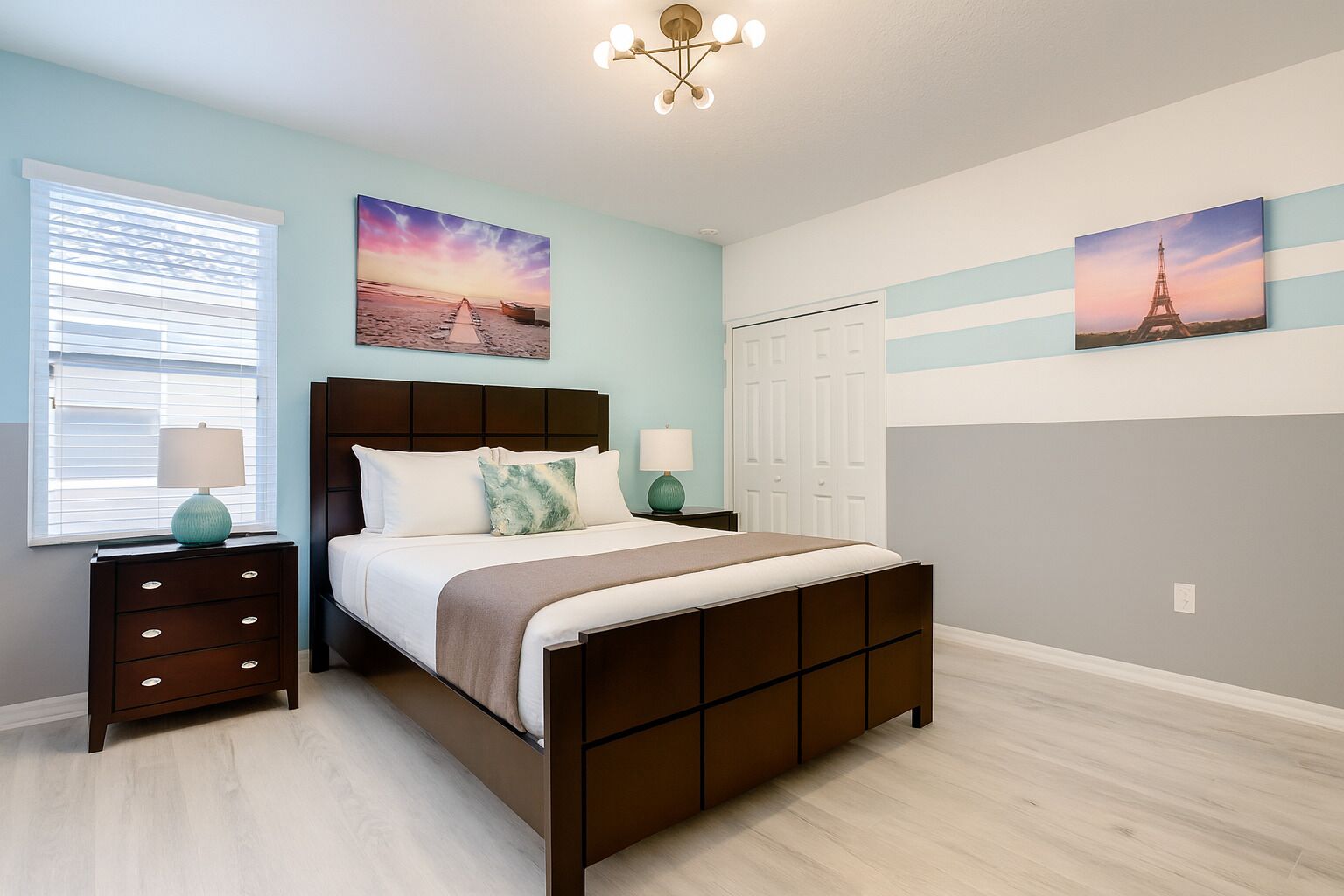 A bedroom with a wooden bed, two bedside tables, a window with blinds, and artwork on the walls.